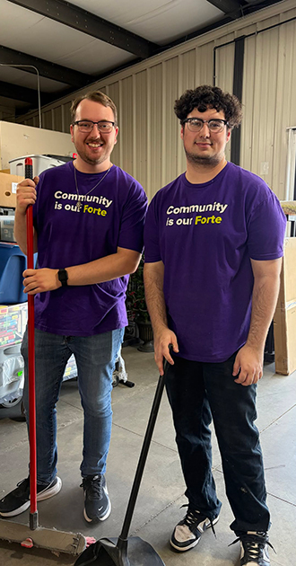 two Forte Bank volunteers in a warehouse holding brooms