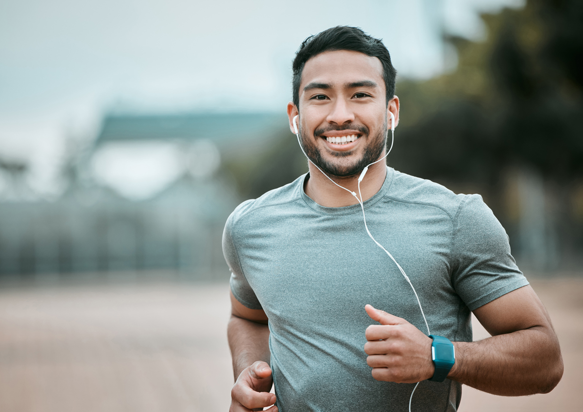 smiling man jogging outdoors with earbuds in