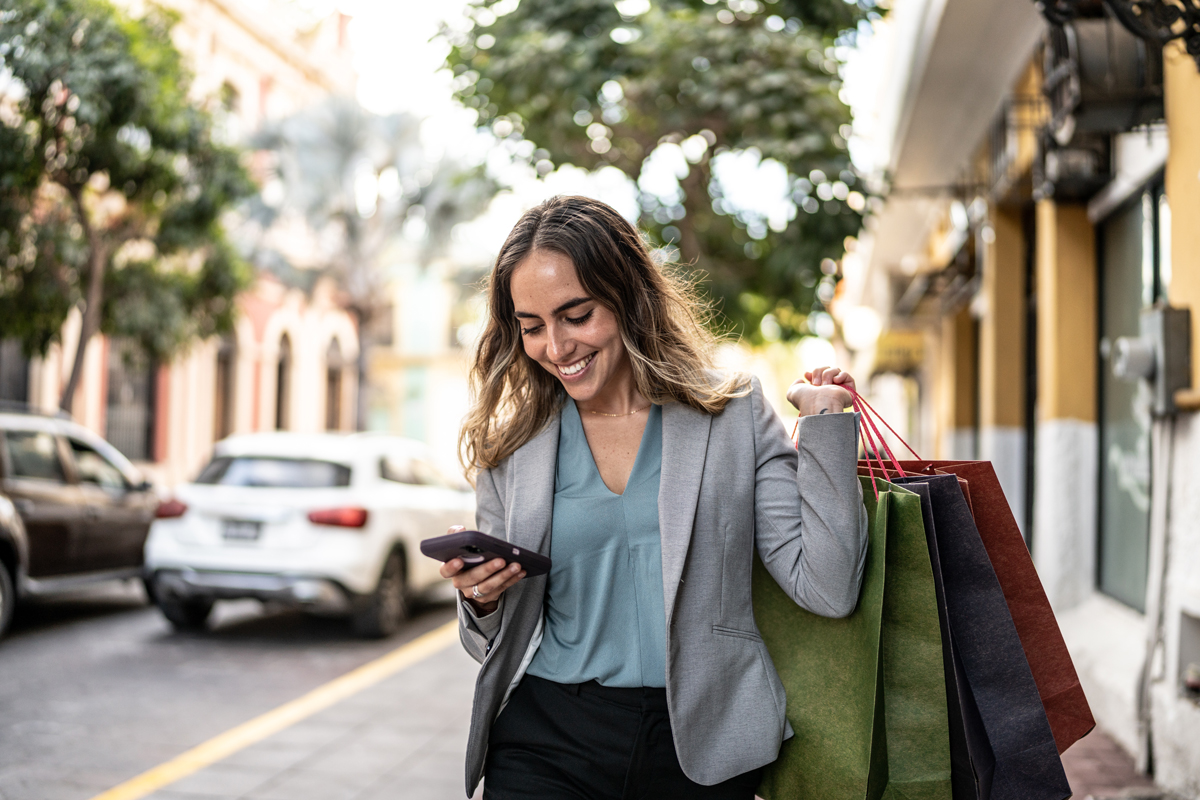 woman outside looking at phone, carrying shopping bags